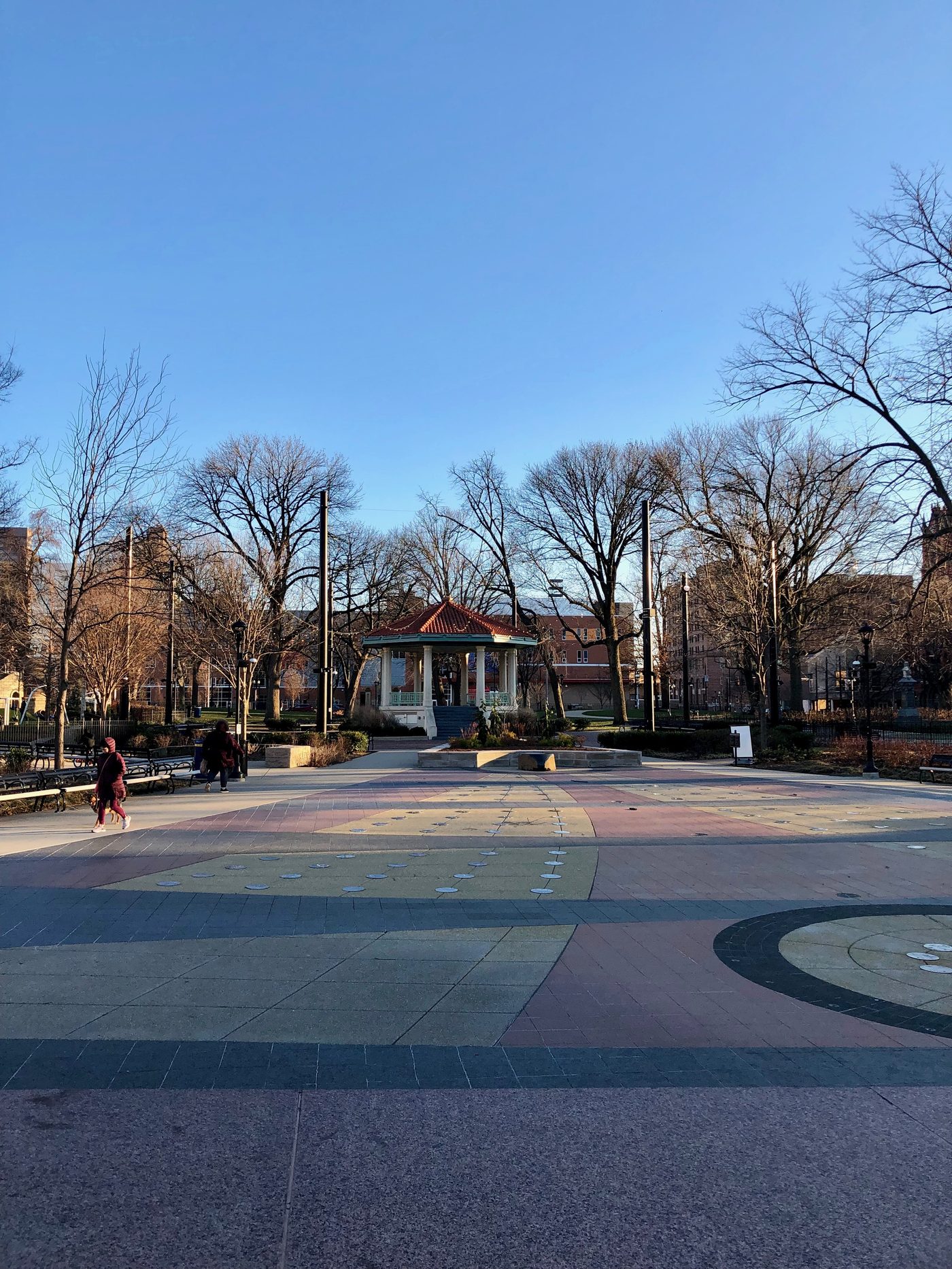 The gazebo and fountain plaza of Washington Park in Cincinnati's Over-the-Rhine; a visitor walks a leashed dog through the park. photo